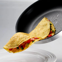 Nonstick fry pan with folded omelet and vegetables, viewed at close angle