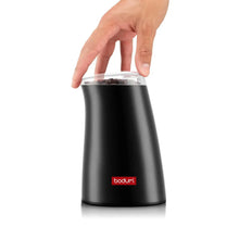 Electric coffee grinder in black with transparent hopper; hand holding the lid