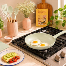 Pale green ceramic non-stick fry pan on stove with two sunny-side eggs