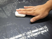 Hand holding a white car clay bar on dark paint with water droplets