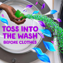 Laundry scent booster beads poured into washing machine drum from green scoop