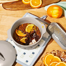 Porcini taupe covered casserole dish with orange slices and dark braised contents