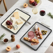 Double-sided cutting board set on a countertop with cheese, bread, and meat.