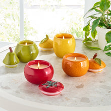 Yellow ceramic lemon candle with lit wick among other fruit-shaped candles