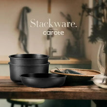Stackable black nonstick pots and bowls set on a wooden countertop