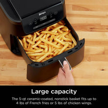 Air fryer with open nonstick basket holding French fries, hand pulling basket