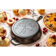 Seasoned cast iron skillet with etched Dolly portrait and two side handles, among dishes