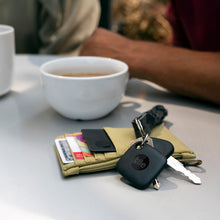 Two black Tile trackers on a keyring with a wallet nearby
