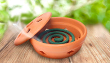 Orange mosquito coil burner on wood with teal spiraled coils and lid