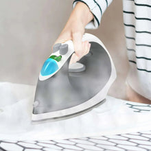 Hand holding a white and gray cordless steam iron steaming fabric on a bed