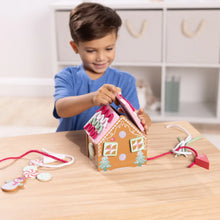 Child attaching lacing ribbons to a pink wooden gingerbread house toy