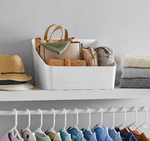 White plastic slanted storage bin holding bags and folded accessories