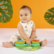 Baby seated with a green musical drum toy featuring three colored drum pads and a jungle frame
