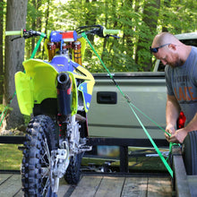 Green tie-down strap with cam buckle being tightened on a motorcycle