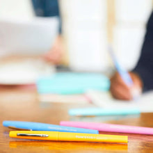 Assorted felt tip pens on a wooden table, blue and pink pens visible