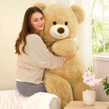 Giant tan teddy bear plush held against the chest, with gold neck bow