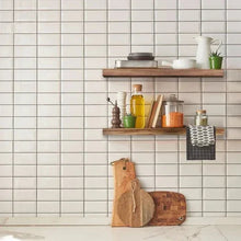 Floating wood shelf mounted on tiled wall with a row of kitchen items