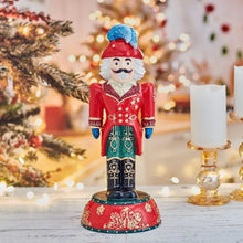 Nutcracker figurine in red coat and blue hat with white beard, arms at sides.