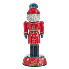 Nutcracker figurine from behind, red jacket with gold accents, blue hat, on red base.
