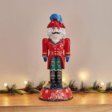 Nutcracker figurine in red coat and blue hat with white beard, standing on red base.
