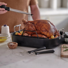 Black nonstick roaster pan with wire rack holding roast chicken