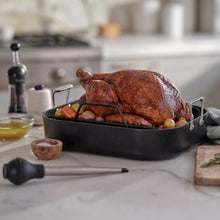 Black nonstick roaster pan with rack holding roast chicken on counter