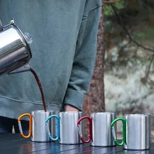 Stainless steel coffee mugs with colorful handles on tabletop