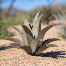 Metal agave yard sculpture with upright spiky leaves, pale gold finish, on stone base