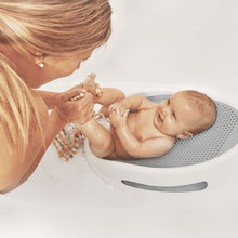 Baby in gray mesh bath support while caregiver holds hands