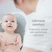 Newborn lying in gray mesh baby bath support on white base
