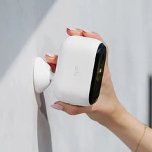 Hand holding a white security camera next to a wall mount bracket