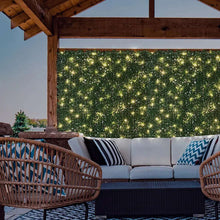Artificial hedge wall panel with warm white lights on a wall, dense green foliage