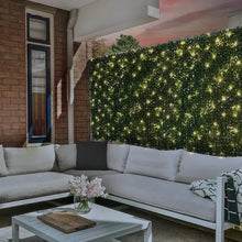 Artificial hedge wall panel with warm white lights, dense green foliage on facade