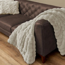 Faux fur throw blanket in light beige with curly pile, folded over sofa arm
