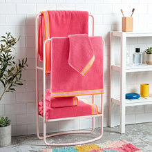 Coral towel set with striped borders, folded on a metal stand