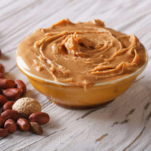 Beige peanut butter powder in bowl with hazelnuts on a wooden surface