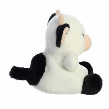 White and black cow plush sitting, with raised ears and black paw pads