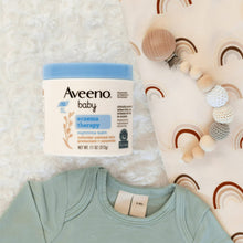 Aveeno baby eczema therapy nighttime balm jar on bedding with baby onesie and toys