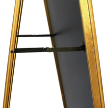 Gold-framed standing mirror with black support bar on the back