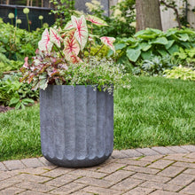 Textured dark gray resin planter with open top outdoors with plants.