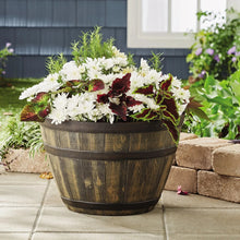 Whiskey barrel resin planter holding white and burgundy flowers on a patio floor