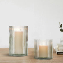 Two green ribbed glass hurricane candle holders with lit candles on a tabletop