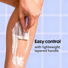 Tapered-handle disposable razor with purple handle, used on leg skin.