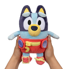 Plush baby Bluey dress toy held up, navy face, light blue body, red overalls with interactive pieces