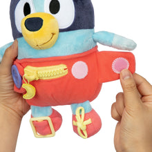 Plush baby Bluey dress toy held by hands, red overalls with round fabric patches and yellow latch
