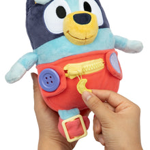 Plush baby Bluey dress toy with red overalls and light blue top; hand pressing detail button