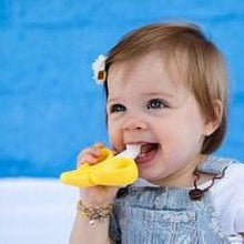 Infant holding yellow banana teether toothbrush with white bristles, smiling