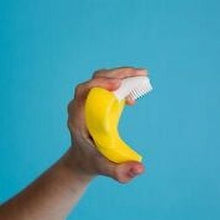 Hand holding yellow banana teether toothbrush with white bristles for infant teeth
