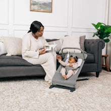 Gray portable baby bouncer with infant seat, used on living room floor