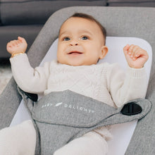 Infant lying in gray portable baby bouncer with safety harness straps